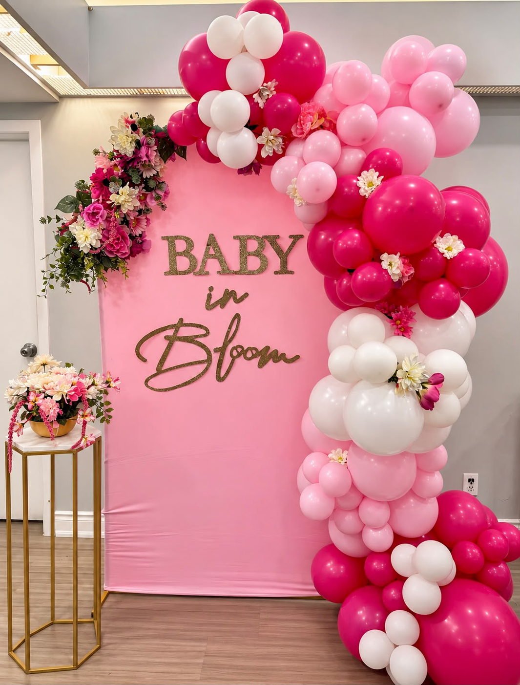 Hot pink Baby in Bloom backdrop with a pink and white balloon garland and gold lettering