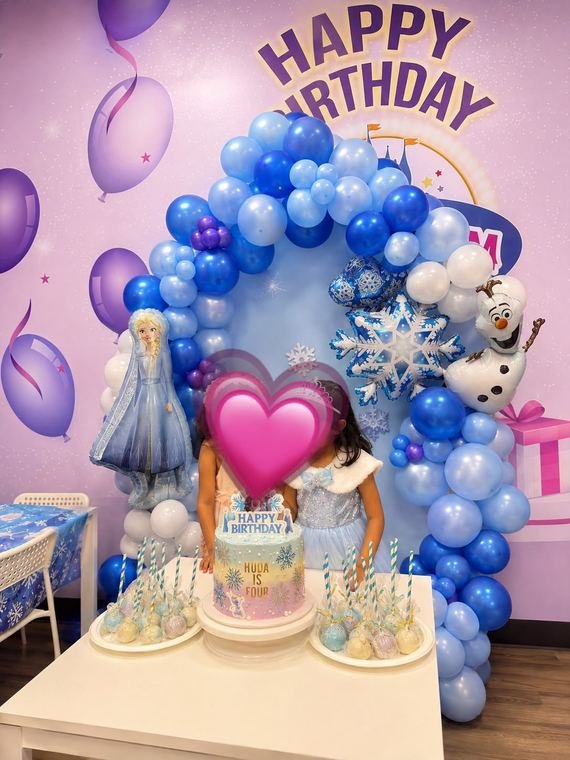 Frozen themed birthday arch in blues, whites and purples with snowflake foils and a dessert table