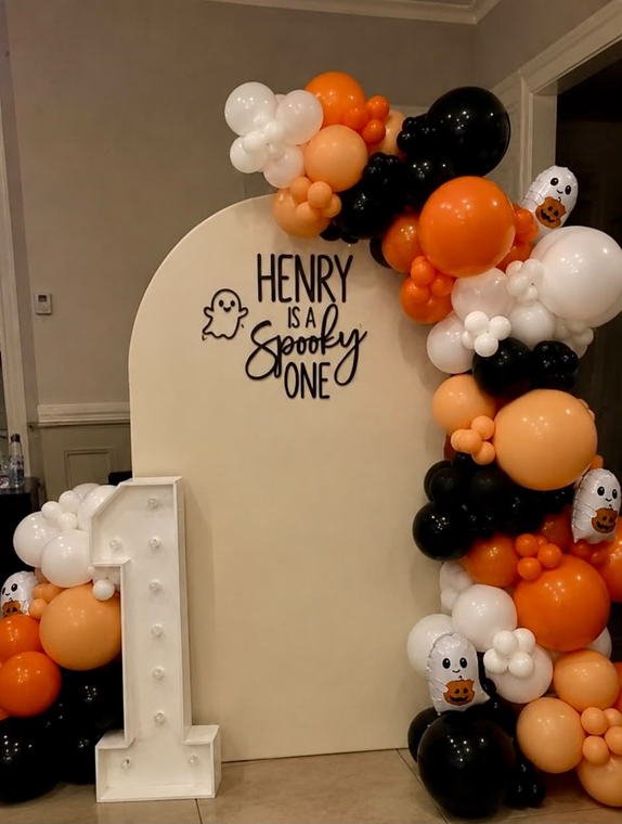 Halloween first birthday backdrop in orange, black and white with ghost foil balloons and a light-up marquee number one